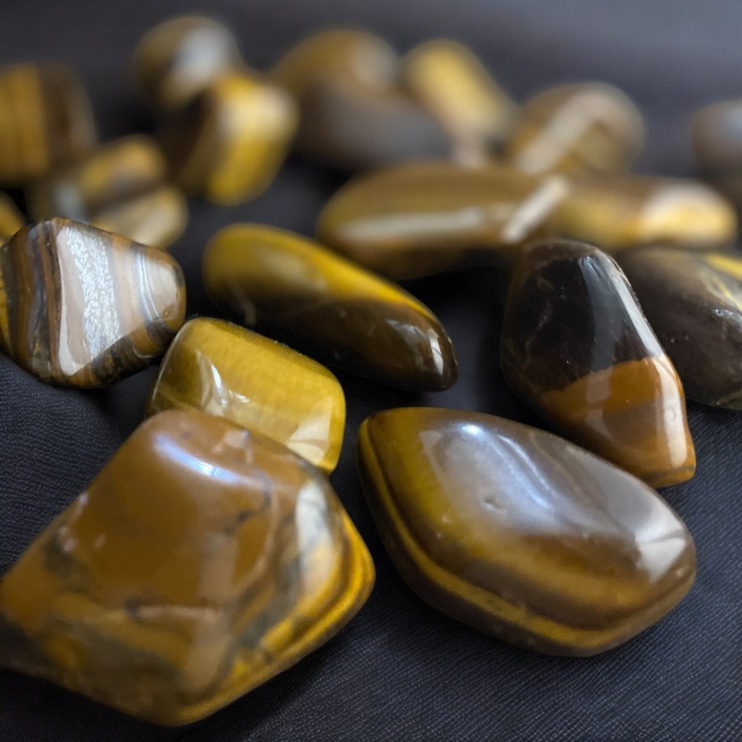 A collection of Tiger Eye tumbled stones with varying shades of yellow, brown, and tan, each with a unique pattern.